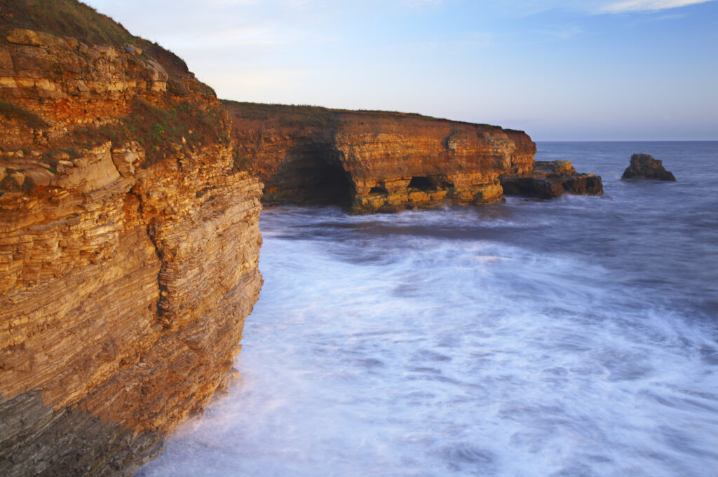 England, Tyne and Wear, Marsden Bay. Early morning light illuminates the crashing waves of the North Sea, near Lizard Point and Marsden Bay.