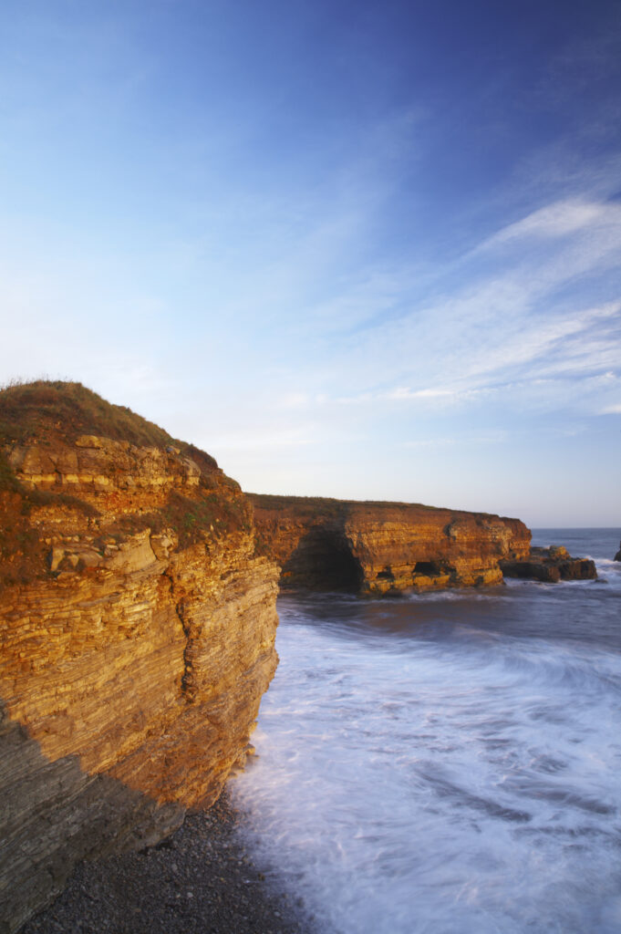 England, Tyne and Wear, Marsden Bay. Early morning light illuminates the crashing waves of the North Sea, near Lizard Point and Marsden Bay.