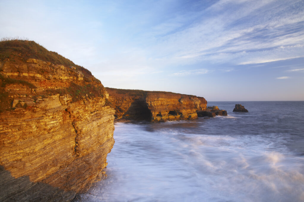 England, Tyne and Wear, Marsden Bay. Early morning light illuminates the crashing waves of the North Sea, near Lizard Point and Marsden Bay.