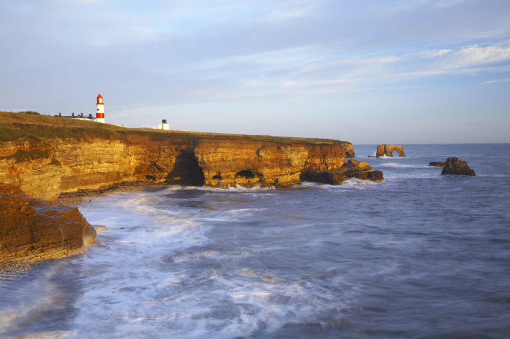 England, Tyne and Wear, Marsden Bay. Early morning light illuminates the crashing waves of the North Sea, near Lizard Point and Marsden Bay.