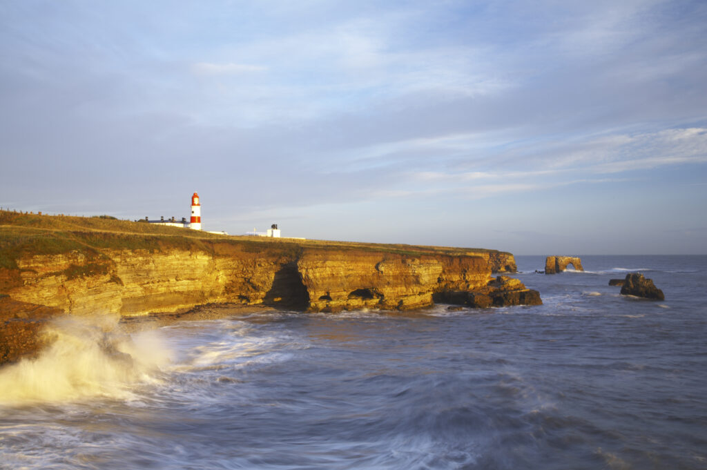 England, Tyne and Wear, Marsden Bay. Early morning light illuminates the crashing waves of the North Sea, near Lizard Point and Marsden Bay.