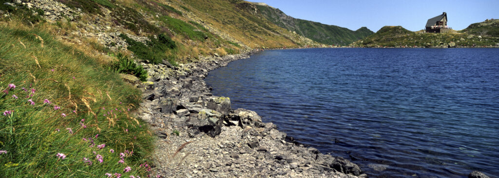 FRANCE, Midi Pyrenees, Pyrenees National Park. The tranquil waters of the Lac d Ilheou with the alpine refuge in the distance