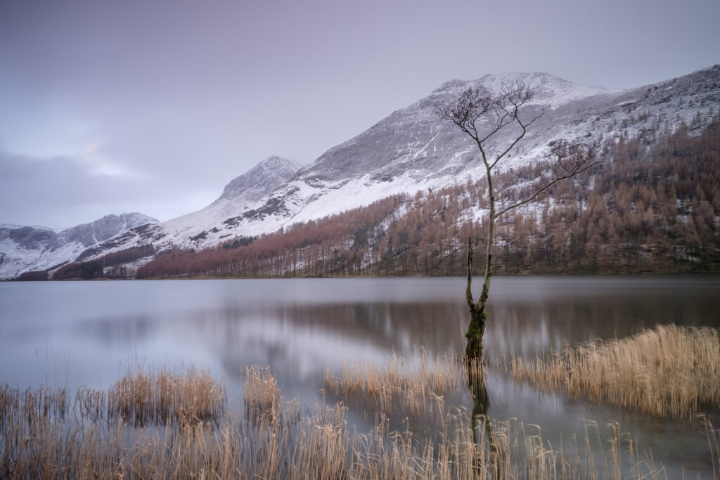 England, Cumbria, Lake District National Park. Snow covered mountains surround the lakeside at Buttermere in the Western Lake District.