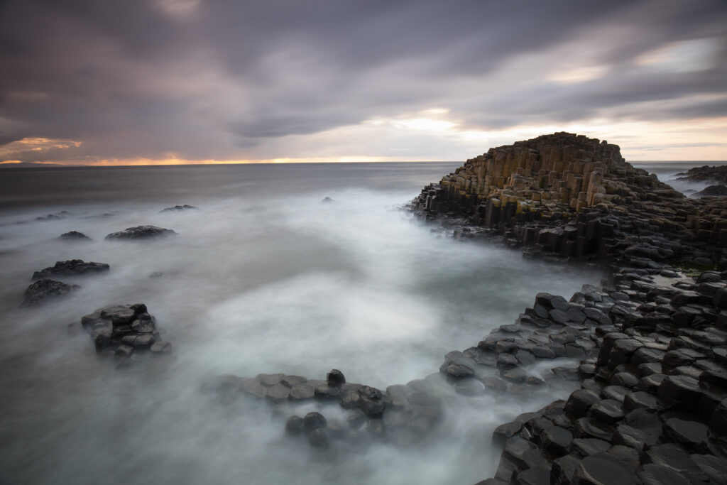 Northern Ireland, Country Antrim, Giant's Causeway. The sun sets behind the hexagonal basalt rock formations of the Wishing Chair, part of the Giant's Causeway Coast World Heritage site.