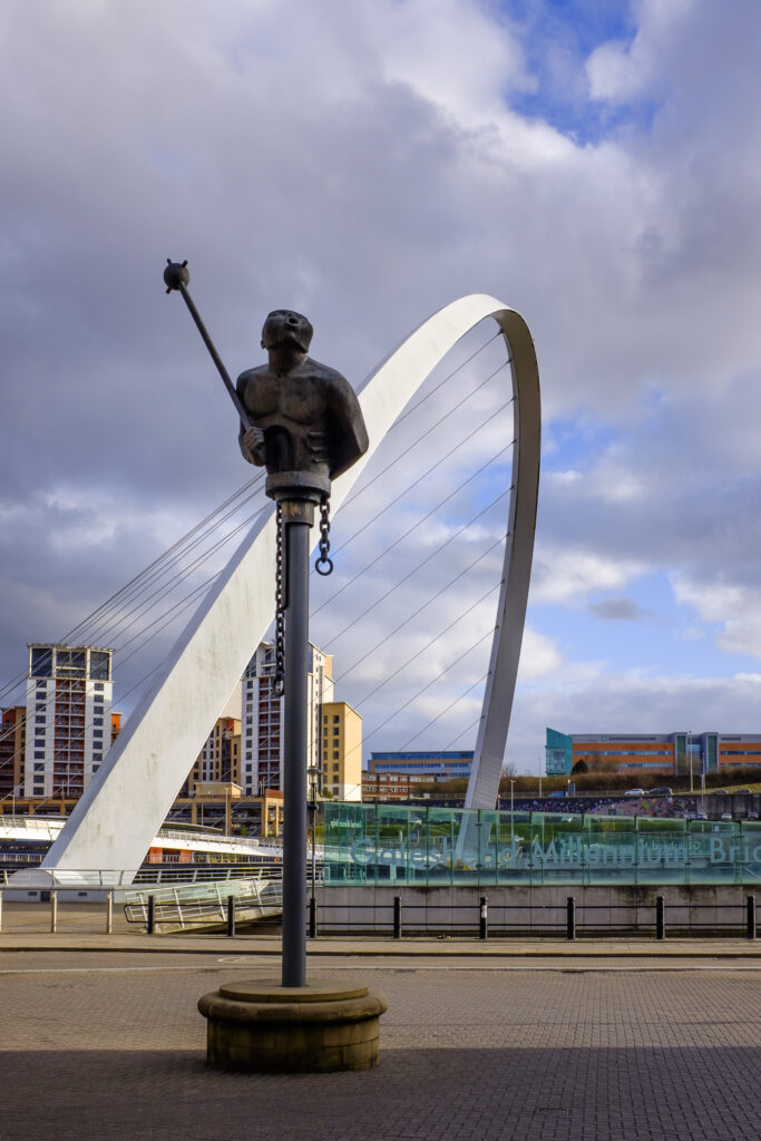 England, Tyne and Wear, Newcastlle Upon Tyne. River God statue with the Gateshead millennium bridge in the distance.