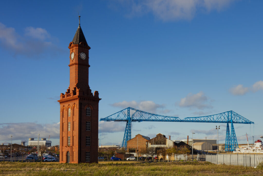 England, Middlesbrough, Middlesbrough Dock Clock Tower. Built in 1903, The Middlesbrough Dock Clock Tower doubled as a clocktower and a watertower to provide the hydraulic power to operate the dock gates and cranes. The Middlesbrough Transporter Bridge can be viewd in the distance.