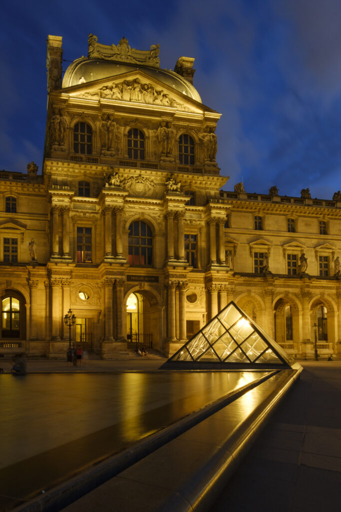 France, Paris, Louvre Museum. The Louvre Museum and Louvre Pyramid (designed by architect Leoh Ming Pei) illuminated at dusk.