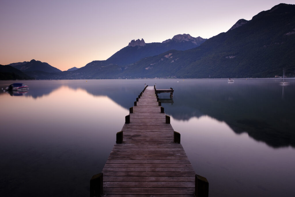 France, Auvergne-Rhône-Alpes, Lake Annecy. Dawn at Lake Annecy, viewed from a lakeside jetty near Doussard looking towards the Teeth of Lanfon on the east banks of the Lac d'Annecy in Haute-Savoie.