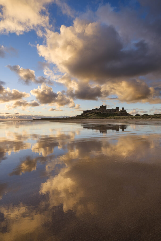 England, Northumberland, Bamburgh. The colours of dawn reflected on the wet, sandy beach at Bamburgh overlooked by Bamburgh Castle, located along the Northumberland Heritage Coast.