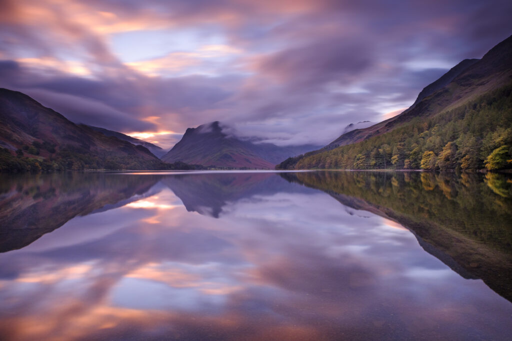 England, Cumbria, Lake District National Park. A colourful autumn sunrise at Buttermere, with Fleetwith Pike reflected in the still waters of the lake.