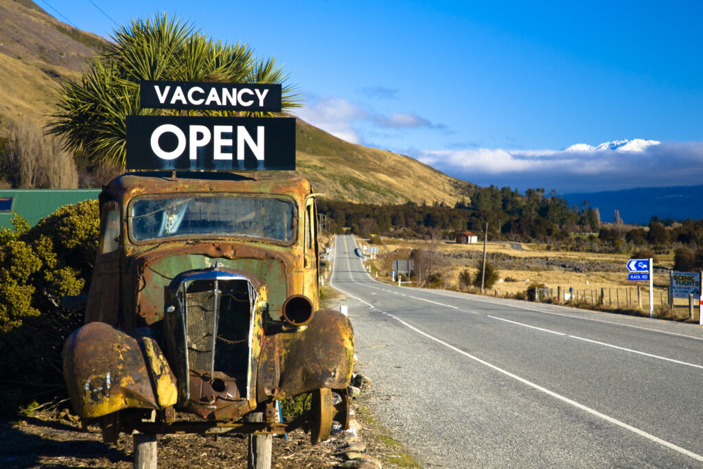 New Zealand, Otago, Makarora. Rusting car used as a hotel 'Vacancy' sign on state highway 6.
