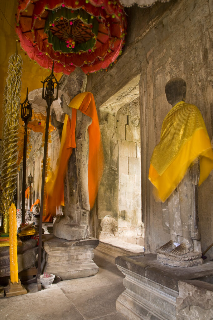 Cambodia, Angkor, Angkor Wat. Buddhist statues colourfully decerated within the dramatic remains of Angkor Wat.
