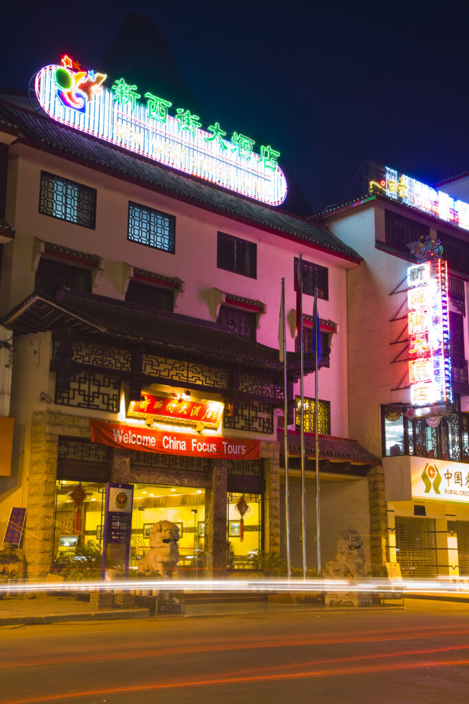 China, Guangxi Zhuang Autonomous Region, Yangshuo City. Busy traffic running through a chinese city at night with a backdop of limestone karst hills.