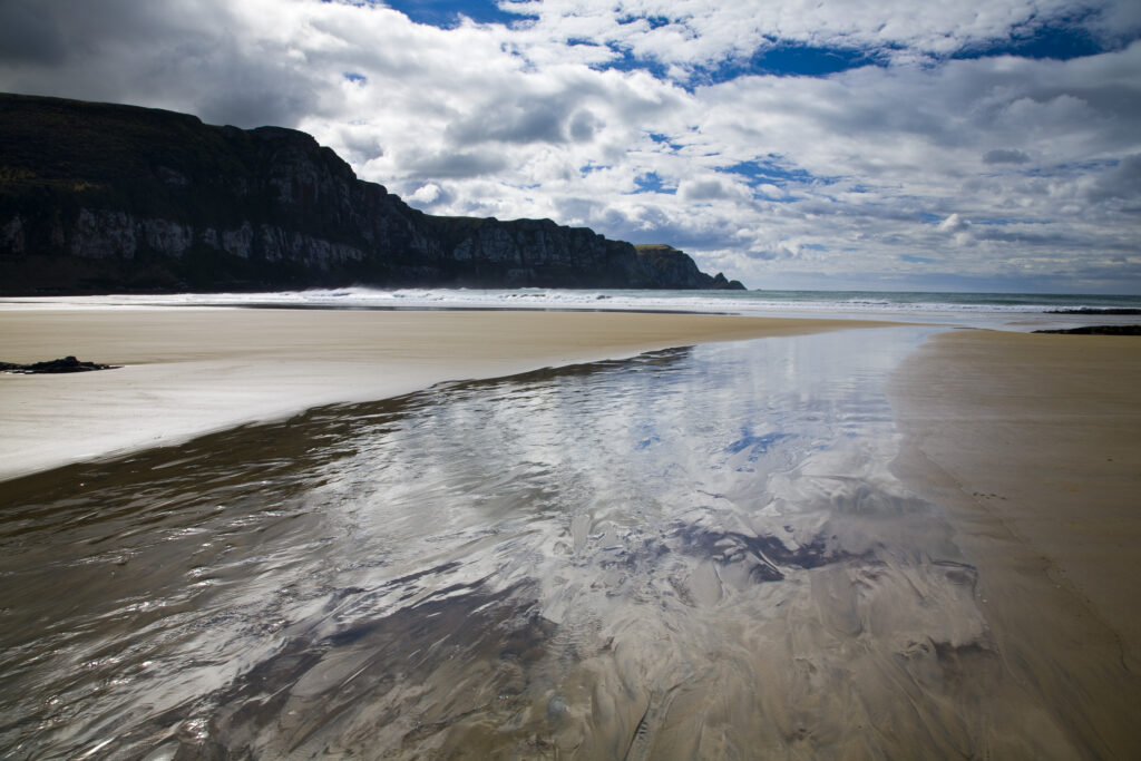 New Zealand, Otago, The Catlins. Tidal stream running accross the sandy beach of Purakaunui Bay.