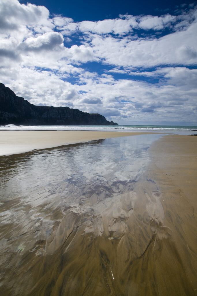 New Zealand, Otago, The Catlins. Tidal stream running accross the sandy beach of Purakaunui Bay.