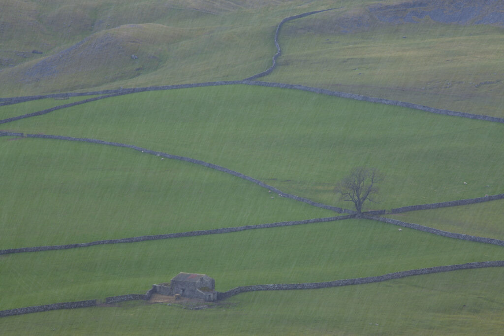 England, North Yorkshire, Yorkshire Dales National Park. Looking down on Crummack Dale during a snow shower and it's traditional dry-stone walls and barn which is a typical feature of the Yorkshire Dales.