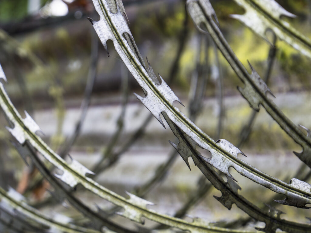 England, West Midlands, Graffiti on wall. Barbed Wire Razor security fence alongside metal fence panel located on an industrial unit near the Stourbridge Canal near Brierley Hill.