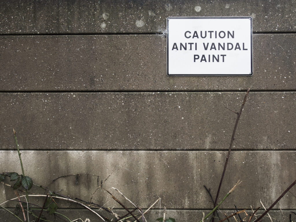 England, West Midlands, Caution Anti Vandal Paint sign on a concrete / cement security fence protecting an industrial unit on the Stourbridge Canal near Brierley Hill.