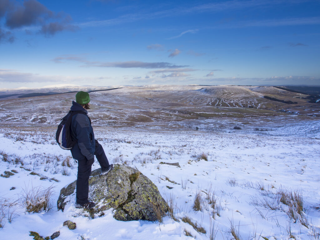England, Northumberland, Northumberland National Park. Hiker taking a break from walking through snow to admire the view of the Cheviot Hills near the Scottish Border and Carter Bar in the Redesdale area of the National Park.