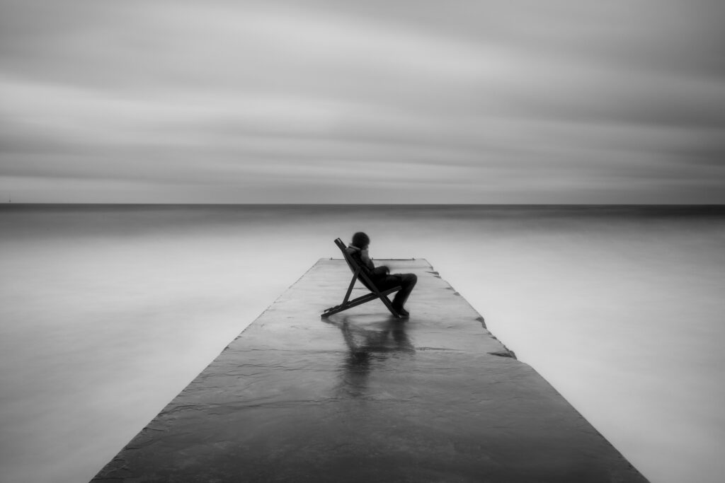 England, Northumberland, Blyth. Person sitting on a deck chair on a jetty during a storm on the Northumberland Coast.