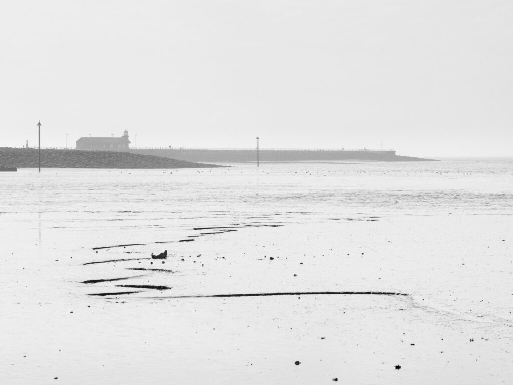England, Lancashire, Morecambe. Sea fog engulfs the stone jetty and lighthouse at Morecambe on Morecambe Bay.