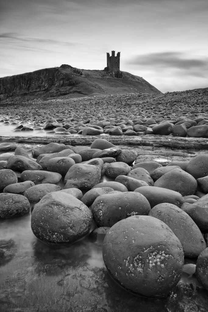 England, Northumberland, Embleton Bay. Sea scultured rocks dominating the coastline of Embleton Bay, overlooked by the dramatic ruins of Dunstanburgh Castle.