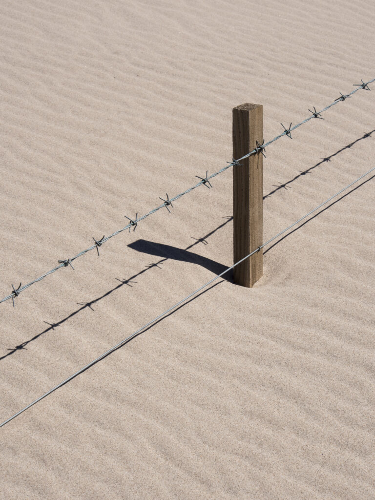 England, Northumberland, Ross Sands. Full height barbed wire fence covered by a drifting sand dune at Ross Sands in Northumberland.