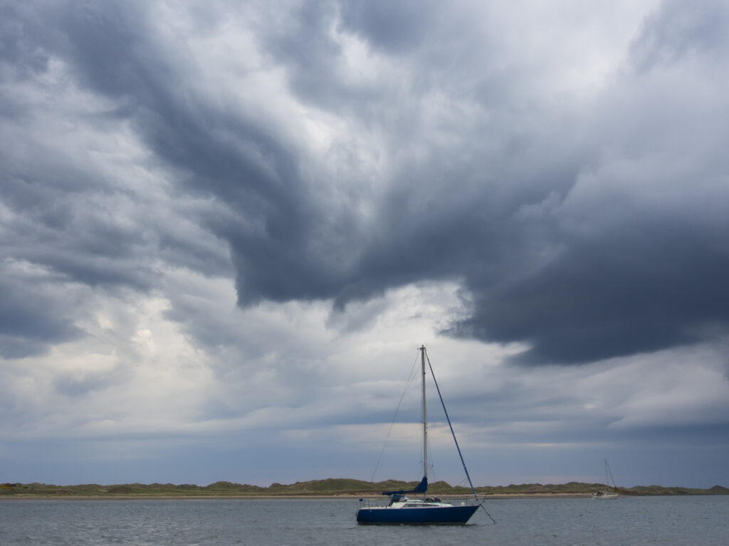 England, Cumbria, Ravenglass. Storm clouds above a boat on the estuary of the river Esk at Ravenglass.