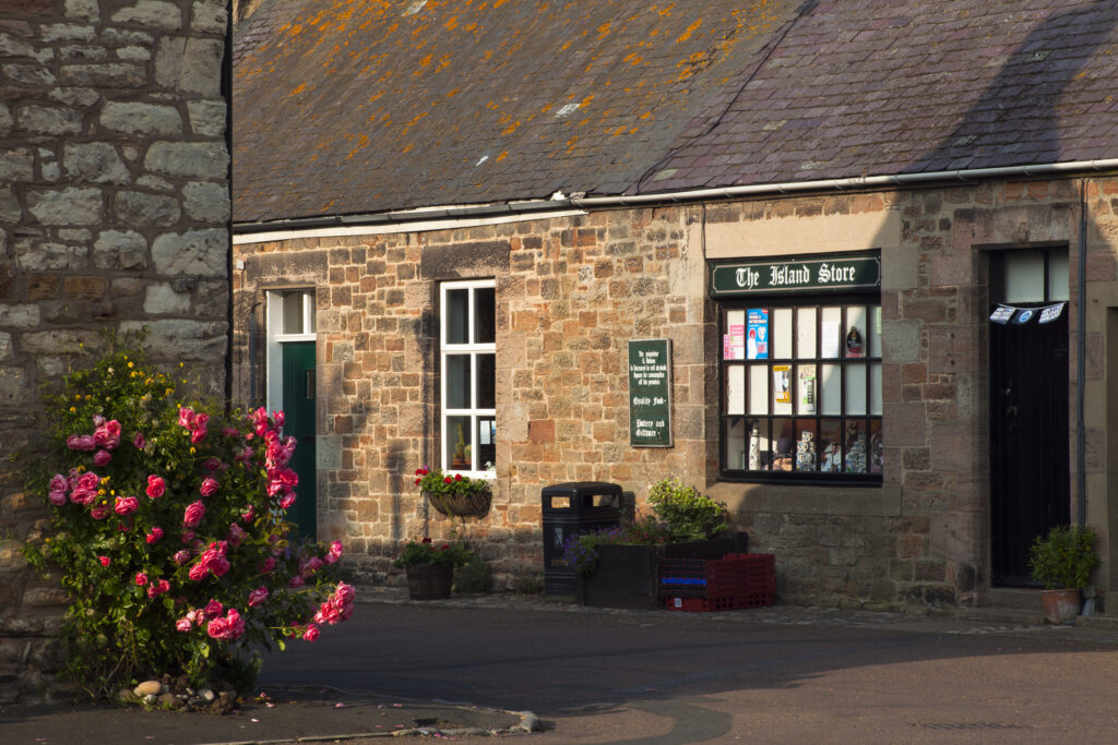 England, Northumberland, Lindisfarne / Holy Island. Summer scene of flowers on a building opposite of the island village store on Lindisfarne