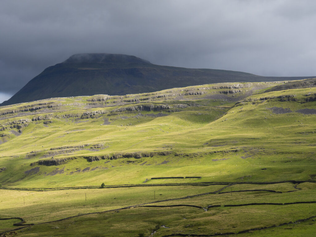 England, Yorkshire, Yorkshire Dales National Park. Storm clouds above a Yorkshire Valley overlooked by Raven Scar and the Ingleborough Mountain.