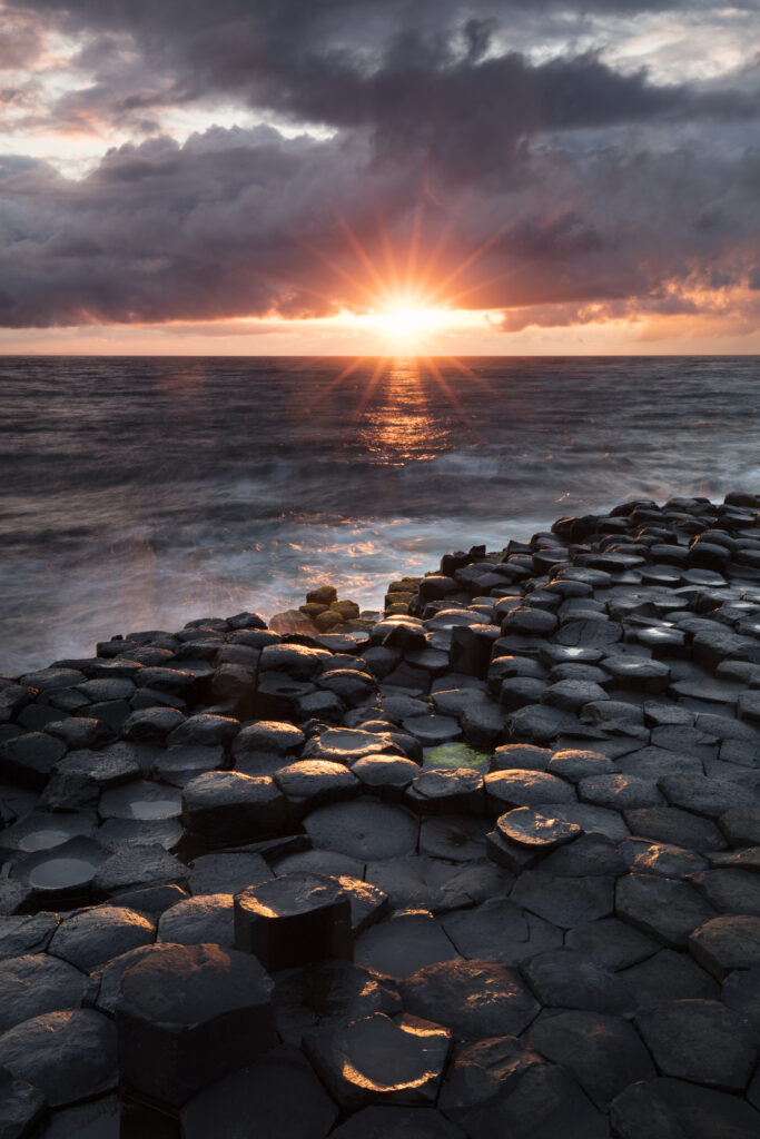 Northern Ireland, Country Antrim, Giant's Causeway. The sun sets behind the hexagonal basalt rock formations of Giant's Causeway Coast World Heritage site.