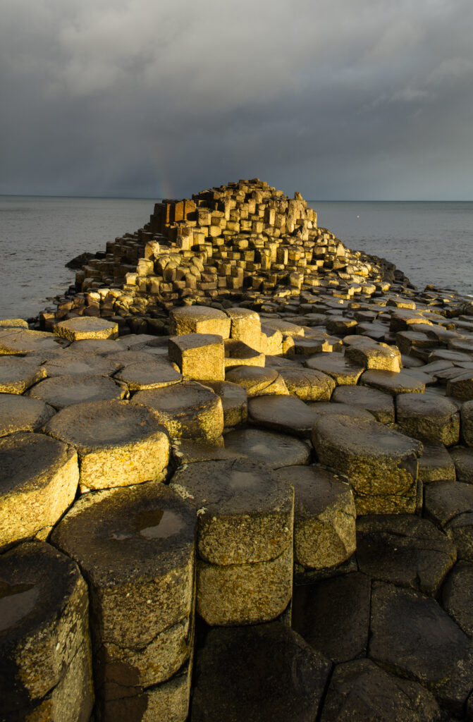 Northern Ireland, Country Antrim, Giant's Causeway. Rainbow behind the hexagonal basalt rock formations of the Wishing Chair, part of the Giant's Causeway Coast World Heritage site.