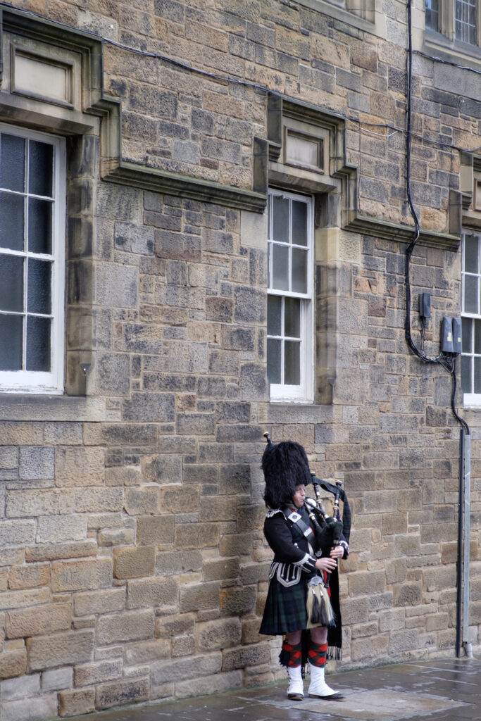 Scotland, Edinburgh, The Royal Mile. Bagpipe player (street performer) playing bag pipes along the Royal Mile in Edinburgh.
