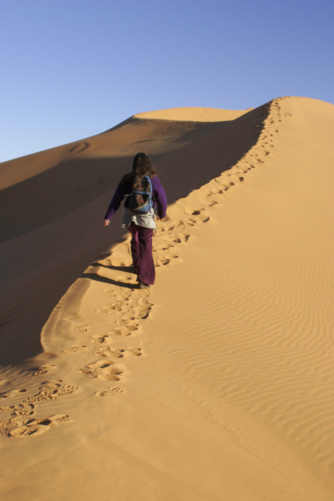 Morocco, Central Morocco, Merzouga. A female tourist backpacker explores the dunes of the Erg Chebbi in the Sahara Desert.