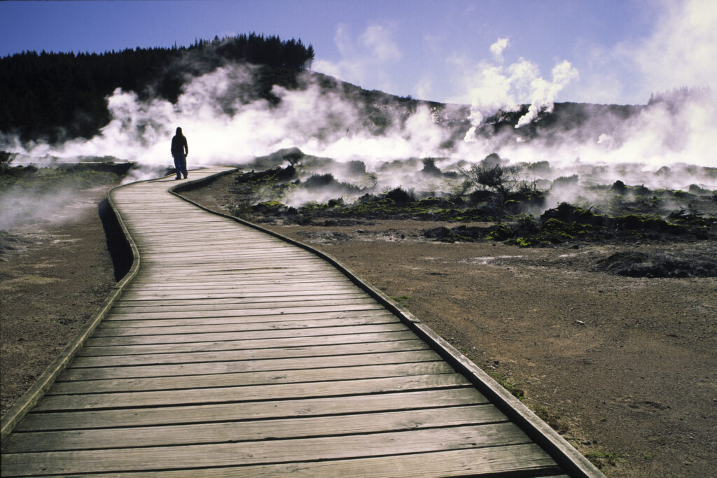 NEW ZEALAND, Central Plateau, Wairakei. Girl standing on boardwalk over steam and thermal activity