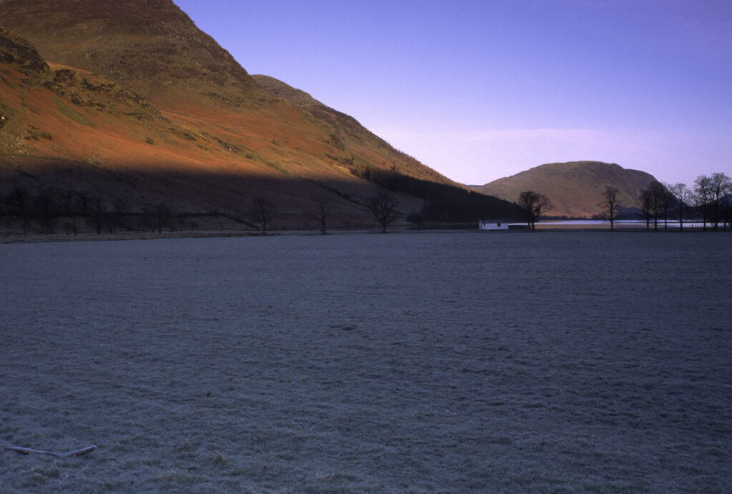 ENGLAND, Cumbria, Lake District National Park. Early morning light illuminates the hills surrounding Lake Buttermere and Peggys Bridge.