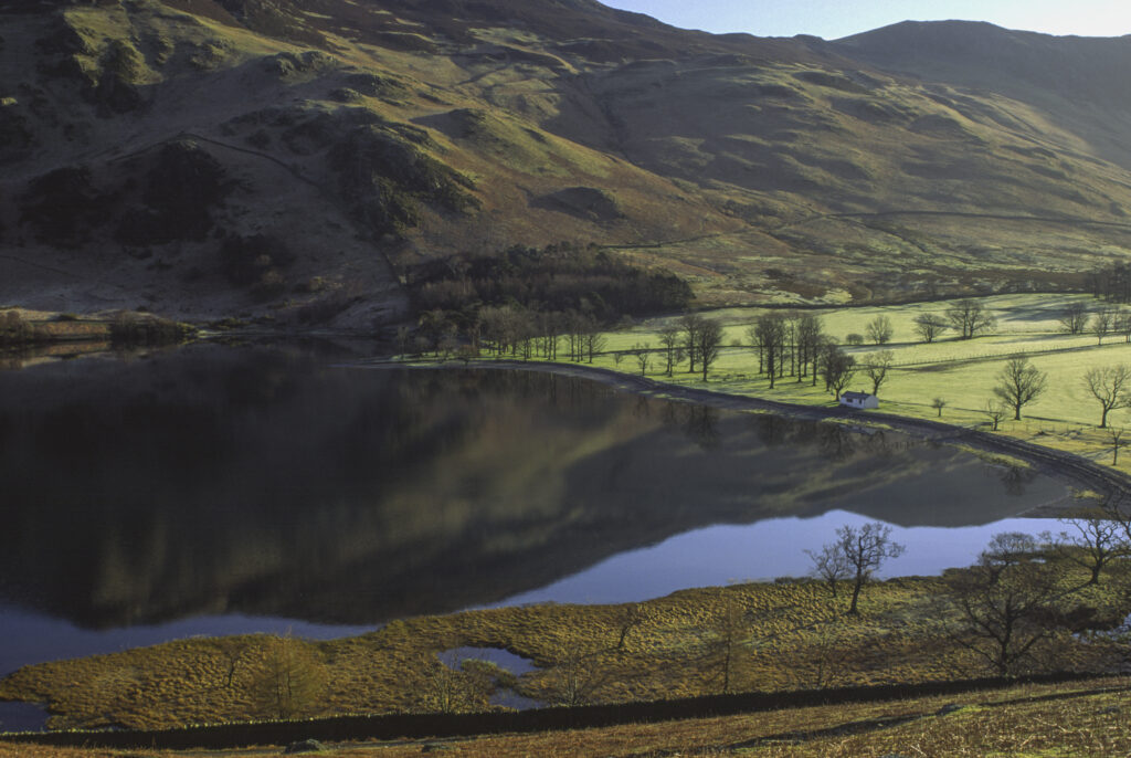 ENGLAND, Cumbria, Lake District National Park. The surrounding mountains reflected in the still waters of Lake Buttermere by Peggys Bridge