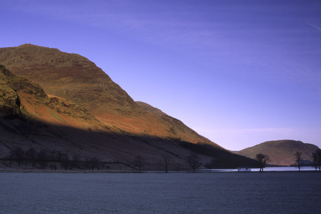 ENGLAND, Cumbria, Lake District National Park. Early morning light illuminates the hills surrounding Lake Buttermere and Peggys Bridge.