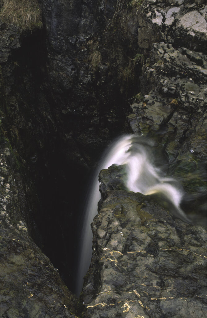 ENGLAND, Yorkshire, Yorkshire Dales National Park. A flowing stream drops into an underground cave system