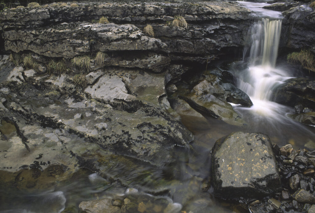 ENGLAND, Yorkshire, Yorkshire Dales National Park. A small waterfall found just before the stream plunges into a cave