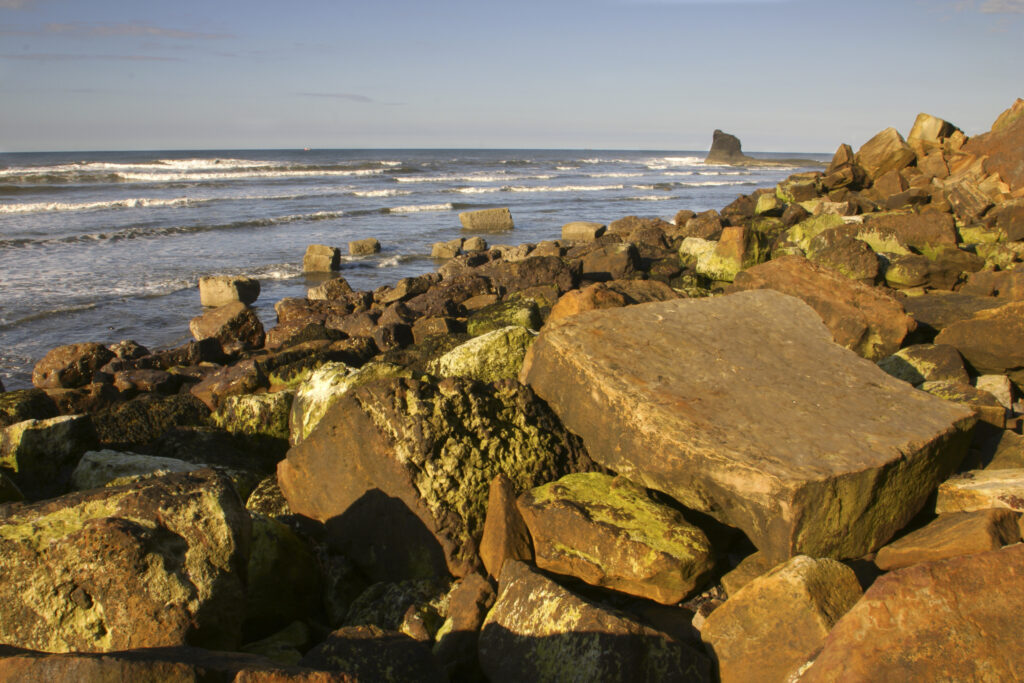 ENGLAND, Yorkshire, North York Moors National Park. Evening light iluminates the boulders of Saltwick Bay near Whitby