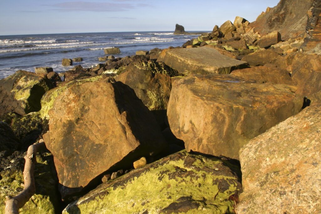 ENGLAND, Yorkshire, North York Moors National Park. Evening light iluminates the boulders of Saltwick Bay near Whitby
