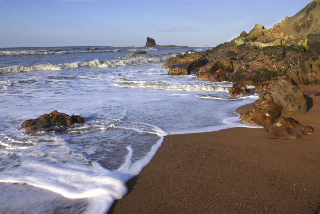 ENGLAND, Yorkshire, North York Moors National Park. Evening light iluminates the boulders and tide of Saltwick Bay near Whitby