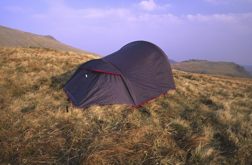 ENGLAND, Cumbria, Lake District National Park. Early evening light illuminates a wild camp spot on the lower slopes of scafell