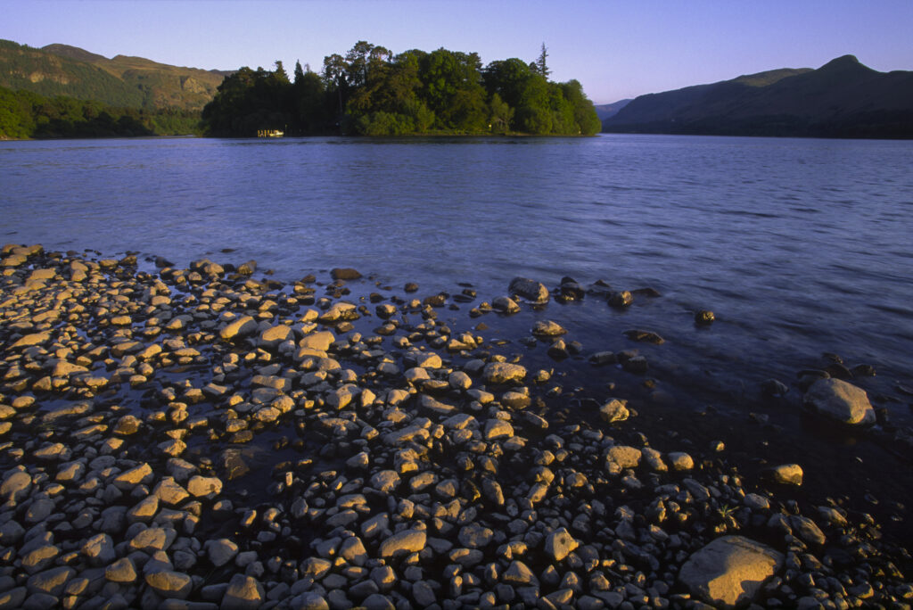 ENGLAND, Cumbria, Lake District National Park. The setting sun illuminates the lakeside and islands of Derwentwater nr Keswick