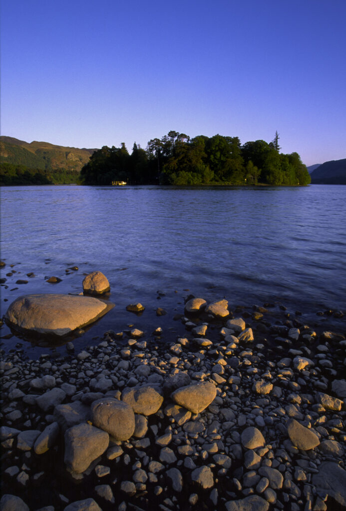 ENGLAND, Cumbria, Lake District National Park. The setting sun illuminates the lakeside and islands of Derwentwater nr Keswick