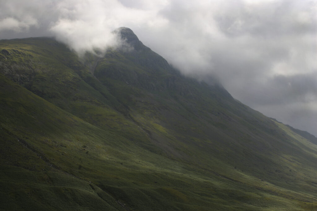 ENGLAND, Cumbria, Lake District National Park. A break in the storm clouds illuminates the Langdale mountains, on the Cumbria Way.