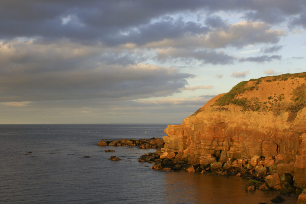 ENGLAND, Tyne & Wear, Tynemouth. The setting sun illuminates the rocky north tyneside coastline near long sands.