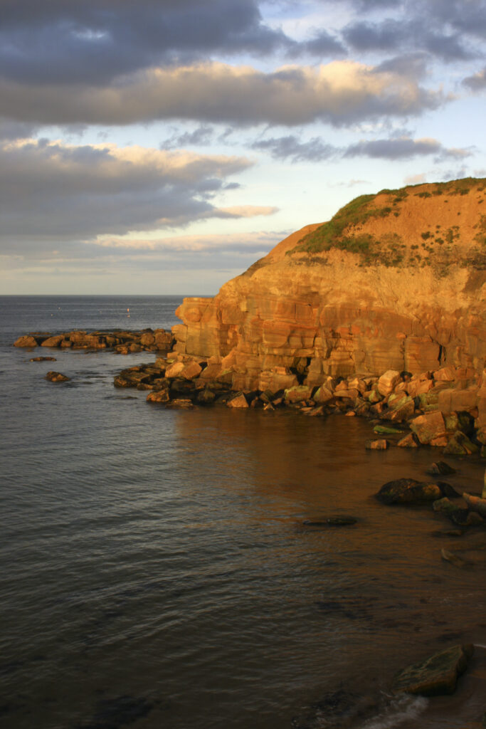 ENGLAND, Tyne & Wear, Tynemouth. The setting sun illuminates the rocky north tyneside coastline near long sands.