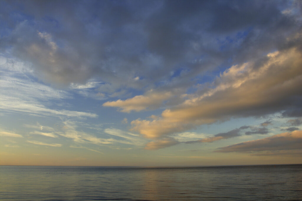 ENGLAND, Tyne & Wear, Tynemouth. The setting sun illuminates the clouds above the vast expanse of the north sea.